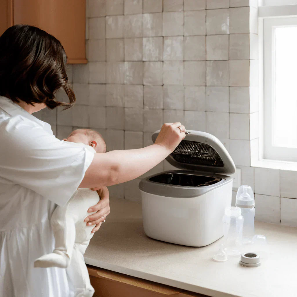 woman holding baby using uv steriliser to clean bottles